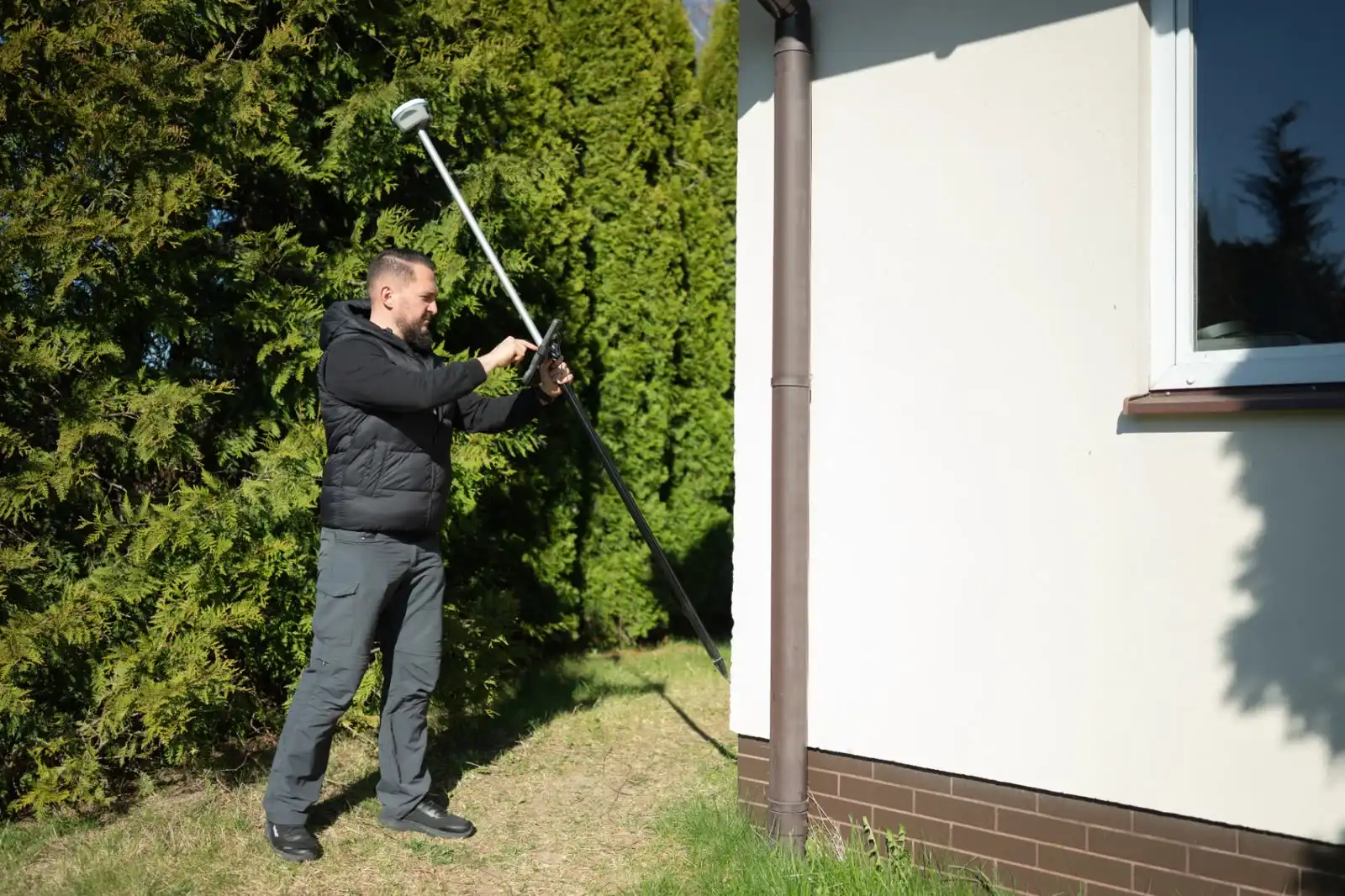 Geodeta wykonujący pomiar inwentaryzacyjny budynku odbiornikiem GNSS na tyczce