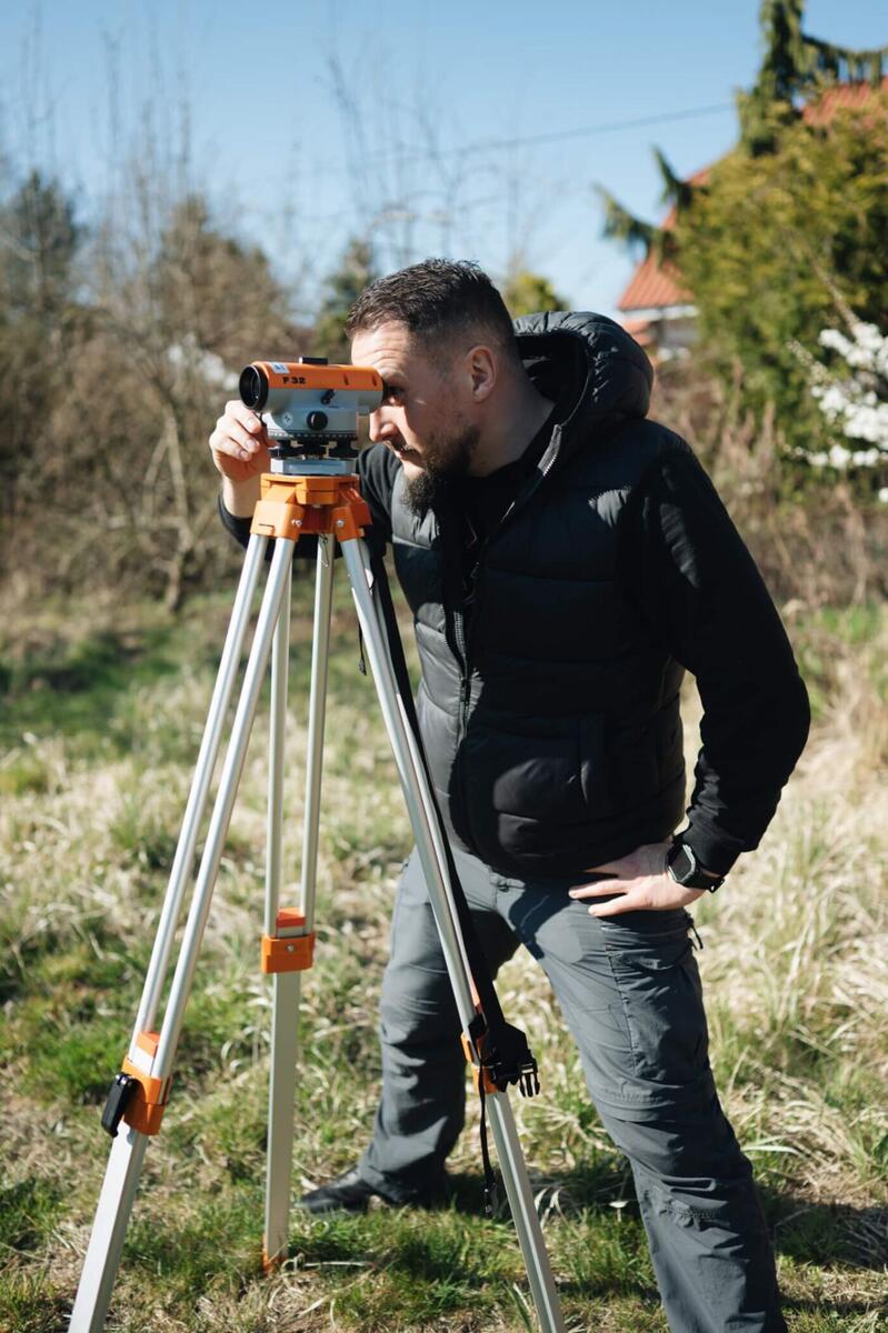 Geodeta wykonujący pomiary niwelatorem optycznym F32